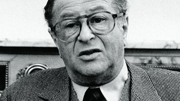 Bruno Kreisky trägt eine Brille, ein gemustertes Sakko sowie eine Krawatte und blickt ernst in die Kamera.
