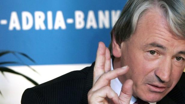 Ein Mann gestikuliert vor einem Banner der Alpe-Adria-Bank.