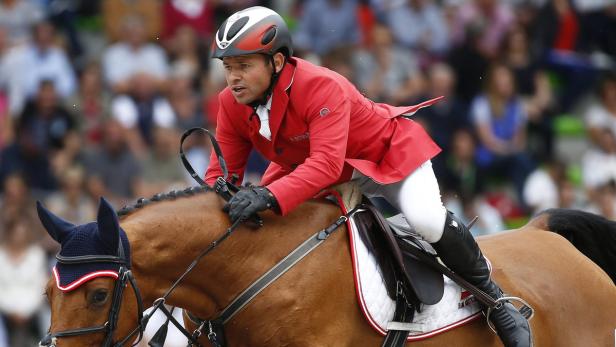 Ein Reiter in roter Jacke auf einem braunen Pferd bei einem Reitturnier.