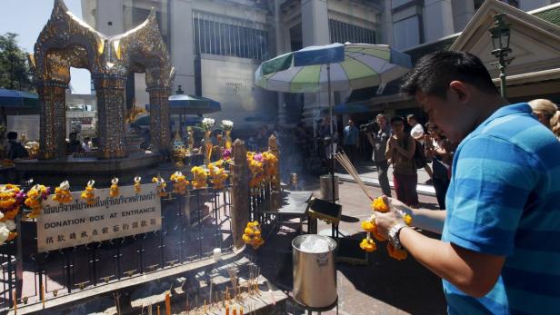Ein Mann zündet Räucherstäbchen und bringt Opfergaben an einem Schrein in Bangkok dar.