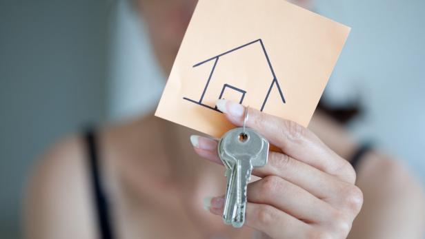 Eine Hand hält einen Schlüssel und einen Zettel mit einer Hauszeichnung.