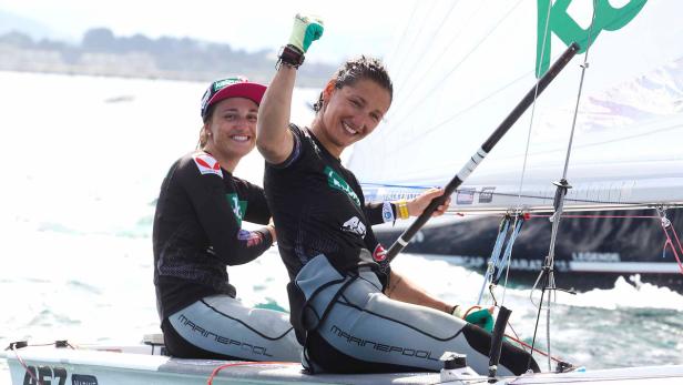 Zwei Seglerinnen jubeln auf einem Segelboot auf dem Wasser.