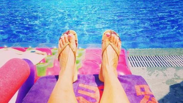 Eine Person entspannt in Flip-Flops auf einer Luftmatratze am Pool.
