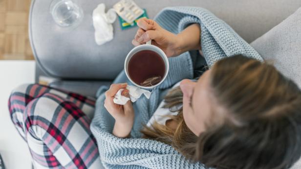 Sick young woman in the bed having hot drink