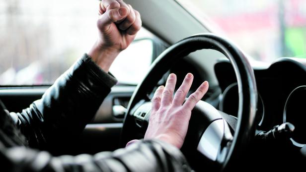 Ein wütender Fahrer ballt die Faust im Auto.