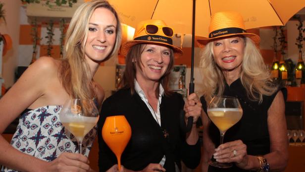 Drei Frauen posieren mit Veuve Clicquot Champagnergläsern und einem orangefarbenen Regenschirm.