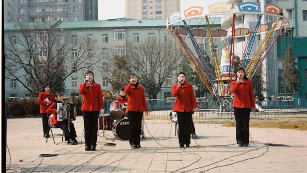 Eine nordkoreanische Musikgruppe tritt vor einem Karussell und Wohngebäuden auf.