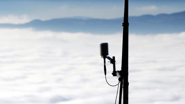 Ein Wettersensor steht vor einer dichten Wolkendecke.