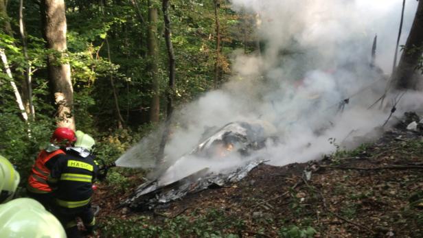 Feuerwehrleute löschen ein brennendes Flugzeugwrack in einem Wald.