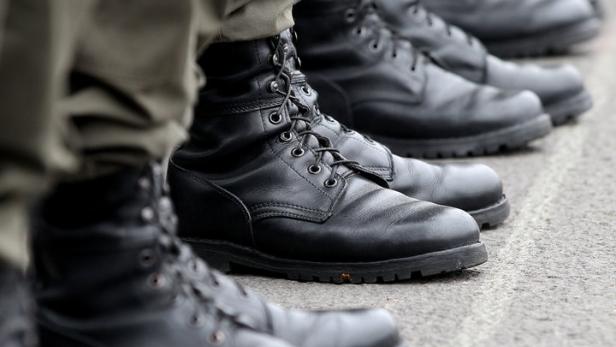 Eine Reihe von Soldaten in Uniform und schwarzen Stiefeln steht stramm.