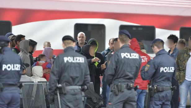 Polizisten stehen vor einer Gruppe von Menschen vor einem Zug.