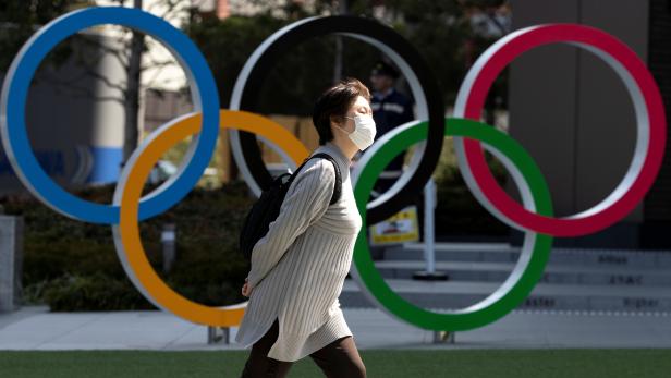 A woman wearing a protective face mask, following an outbreak of the coronavirus disease (COVID-19), walks past the Olympic rings in front of the Japan Olympics Museum in Tokyo