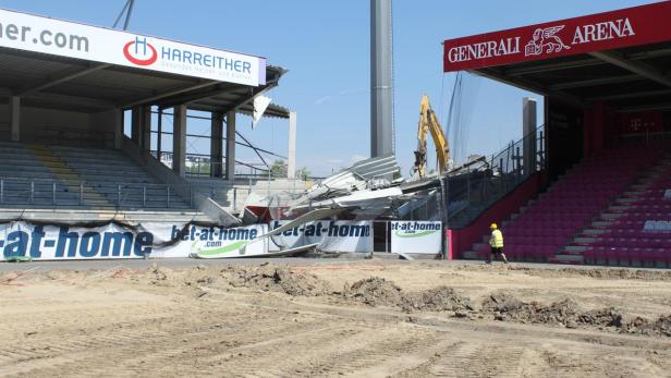 Ein Bagger demoliert einen Teil der Generali Arena, während ein Arbeiter vorbeigeht.