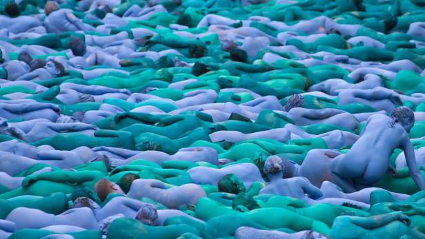 Viele mit blaugrüner Farbe bemalte, nackte Menschen liegen dicht nebeneinander.