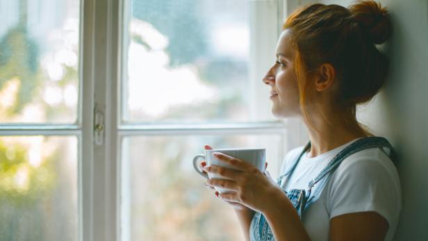 Young beautiful woman is looking through the window and drinking coffee in the morning