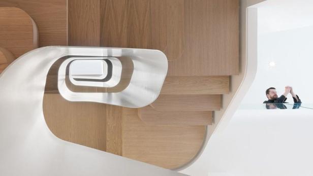Eine moderne Holztreppe mit einem Geländer aus gebogenem, weißem Metall. Im Hintergrund steht eine Person.