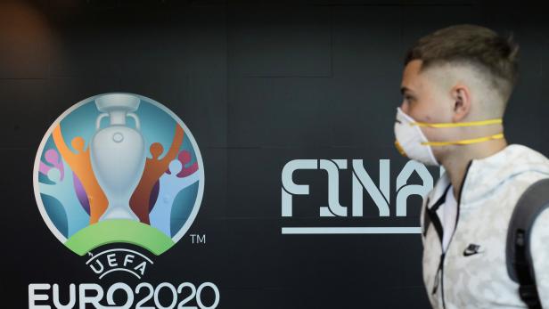 Travellers pass by a logo of the 2020 UEFA European Football Championship displayed on a wall inside Bucharest Henri Coanda International Airport