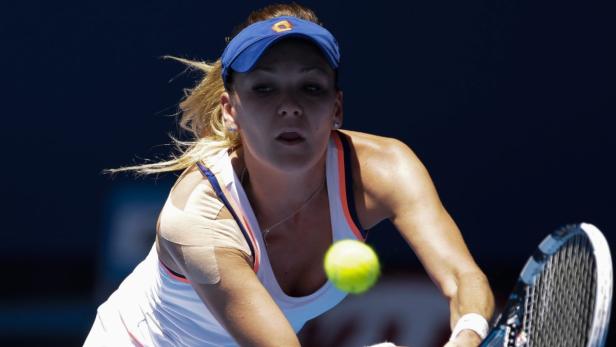 Eine Tennisspielerin schlägt einen gelben Tennisball.