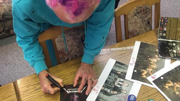 Eine Person mit pinken Haaren signiert ein Metallica-Album mit einem roten Stift.