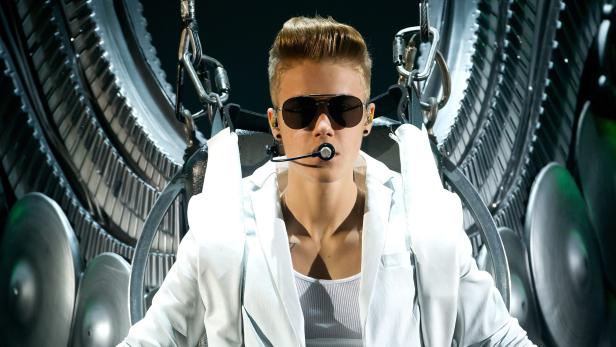 Justin Bieber sitzt in einem futuristischen Stuhl mit Klaviertasten und Becken im Hintergrund.