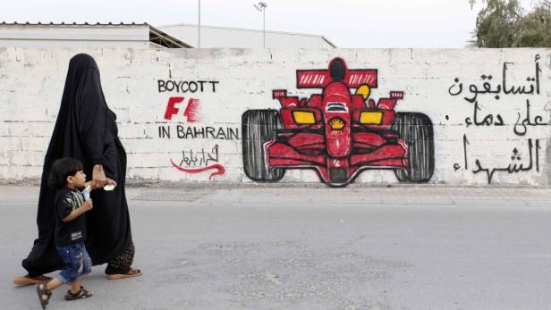 Eine Frau in Abaya geht mit einem Kind an einer Wand mit Graffiti vorbei, die zum Boykott der Formel 1 in Bahrain aufrufen.