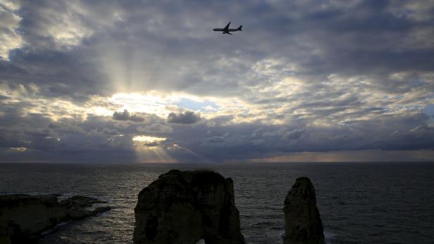 An airplane flies over the Pigeons' Rock as storm clouds loom during sunset in Beirut
