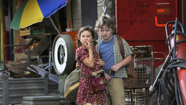 Ein Mädchen und ein Junge stehen vor einem Laden mit einer Waage und einem Sonnenschirm.