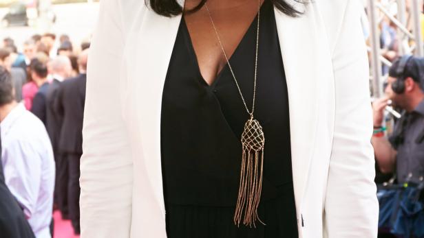 Eine Frau in einem schwarzen Overall und einem weißen Blazer auf einem roten Teppich.