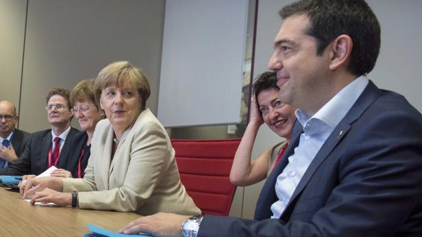 Angela Merkel und Alexis Tsipras sitzen mit anderen Personen an einem Tisch.