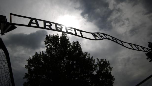Das Tor mit der Aufschrift „Arbeit macht frei“ in Auschwitz vor einem bewölkten Himmel.