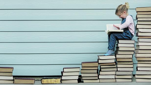 Young girl sits on stack of books