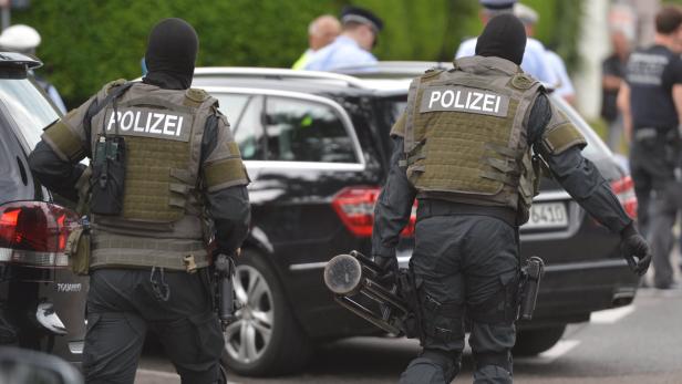 Zwei Polizisten in Kampfmontur stehen neben schwarzen Autos.