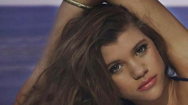 Porträt einer jungen Frau mit braunen Haaren und einem Arm über dem Kopf.