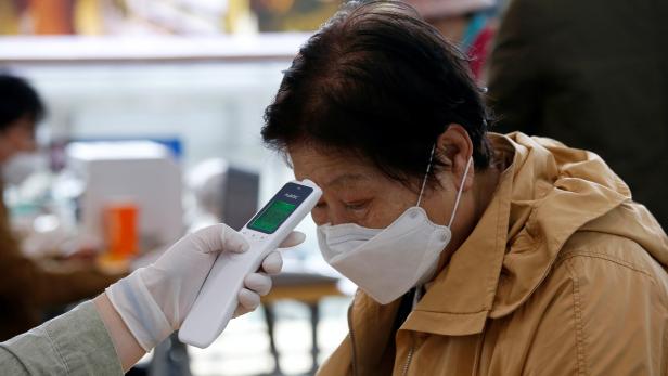 A woman wearing a preventive face mask has her temperature checked at a polling station in Seoul