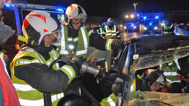Feuerwehrleute arbeiten mit hydraulischem Rettungsgerät an einem verunfallten Auto.