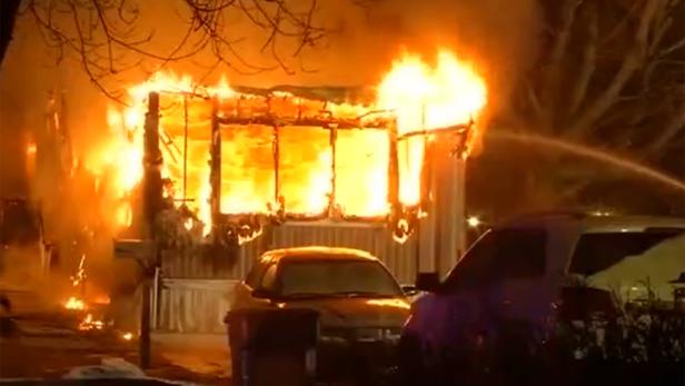 Ein Haus steht in Flammen, während zwei Autos davor geparkt sind.