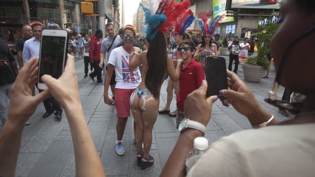 Eine Frau mit Federschmuck und aufgemalten Buchstaben „NY“ posiert für Fotos am Times Square.