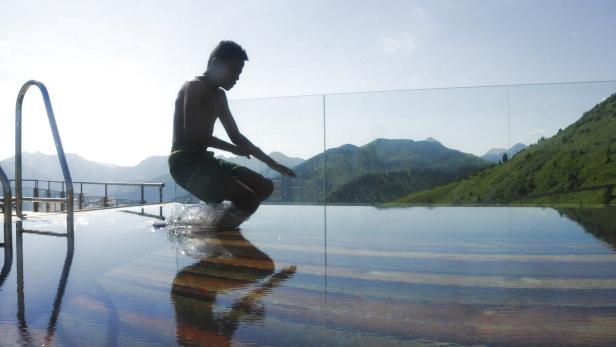 Ein junger Mann springt in ein Schwimmbad mit Bergblick.