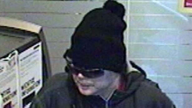 Eine Person mit Sonnenbrille und Mütze steht vor einem Automaten.