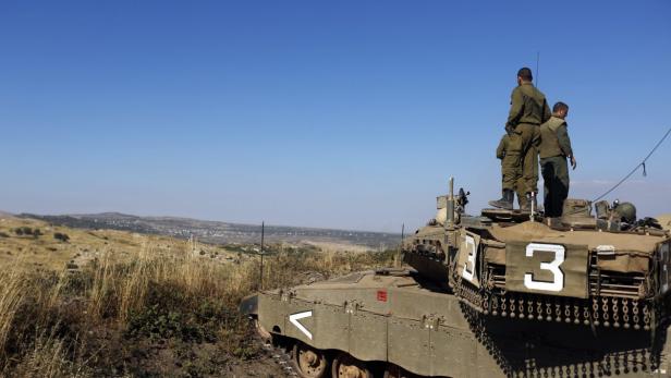 Soldaten stehen auf einem Panzer in einer hügeligen Landschaft.