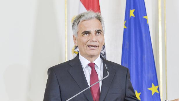 Ein Mann in einem Anzug spricht vor Flaggen Österreichs und der Europäischen Union.