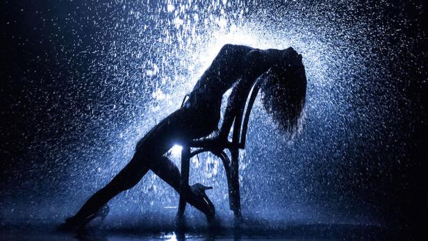 Eine Frau tanzt im Stil von „Flashdance“ (1983) im Regen auf einem Stuhl.