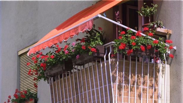 Ein Balkon mit roter Markise und üppigen Geranienkästen.