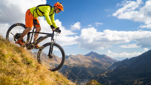 one mountain biker cycling down steep pasture high up in mountains