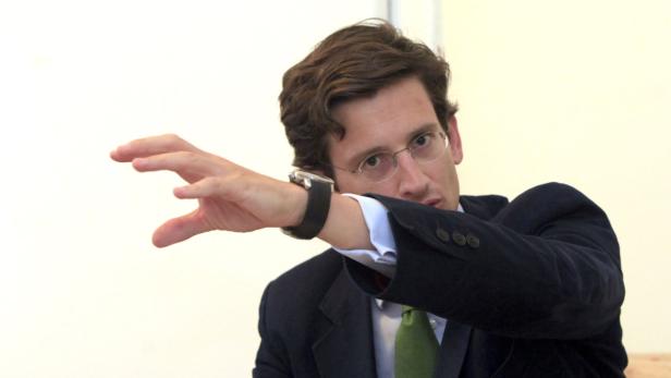 Ein Mann mit Brille und Anzug streckt die Hand aus.