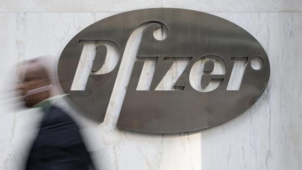 Ein Mann geht an einem großen Pfizer-Logo vorbei.