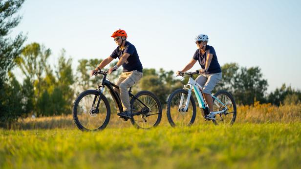 active senior couple cycling on mountain bikes through rural landscape