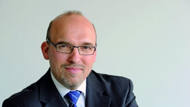 Ein Mann mit Brille, Anzug und Krawatte lächelt in die Kamera.