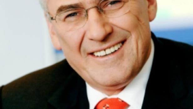 Ein lächelnder Mann mit Brille und Anzug mit roter Krawatte.