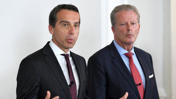 Zwei Männer in Anzügen stehen vor einer hellen Wand.